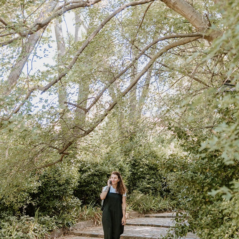 Femme au téléphone dans un jardin luxuriant Femme souriante parlant au téléphone en descendant un sentier de pierres sous des arbres feuillus et verts en pleine nature.